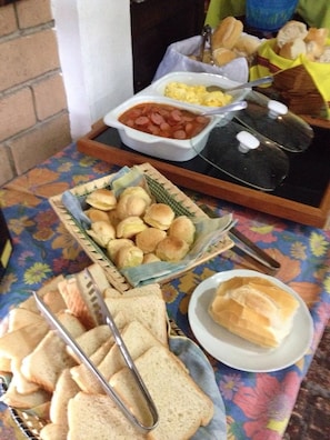 A table with a variety of food items including bread, rolls, and a dish with eggs and tomatoes. - Barequeçaba Praia Hotel (São Sebastião)