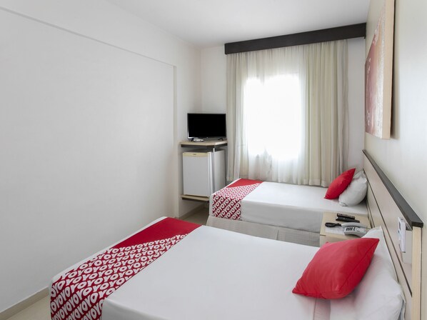 A hotel room with two beds, a desk with a TV, and a window with curtains.
