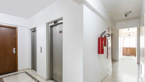 A hallway with two elevators, a fire extinguisher, and a wooden door. - Polo Hotel (São José dos Campos)