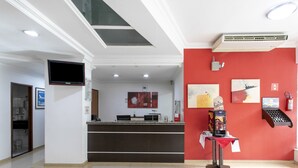 A hotel reception area with a modern design, including a reception desk, a coffee machine, and artwork on the walls. - Polo Hotel (São José dos Campos)