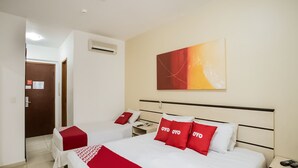 A hotel room with two beds, a red and white bedspread, a red pillow with "OYO" text, a wall-mounted air conditioner, and a painting above the beds. - Polo Hotel (São José dos Campos)