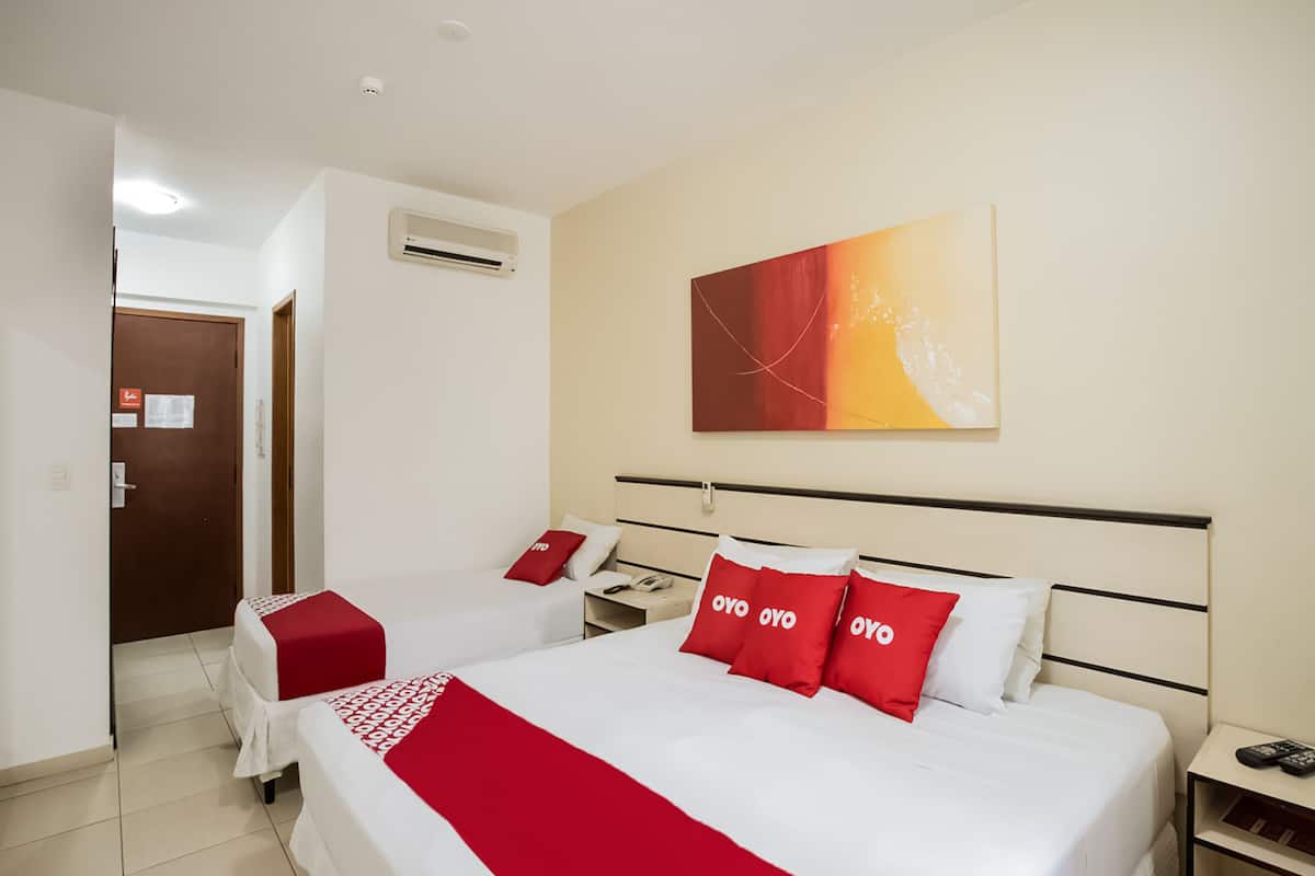 Una habitació d'hotel amb dos llits, un edredó vermell i blanc, un coixí vermell amb el text "OYO", aire condicionat fixat a la paret i un quadre damunt dels llits.