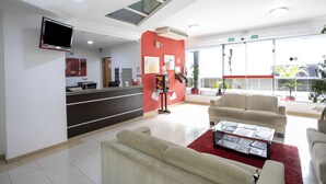 A modern reception area with a reception desk, seating area, and a large window offering a view of the outside. - Polo Hotel (São José dos Campos)