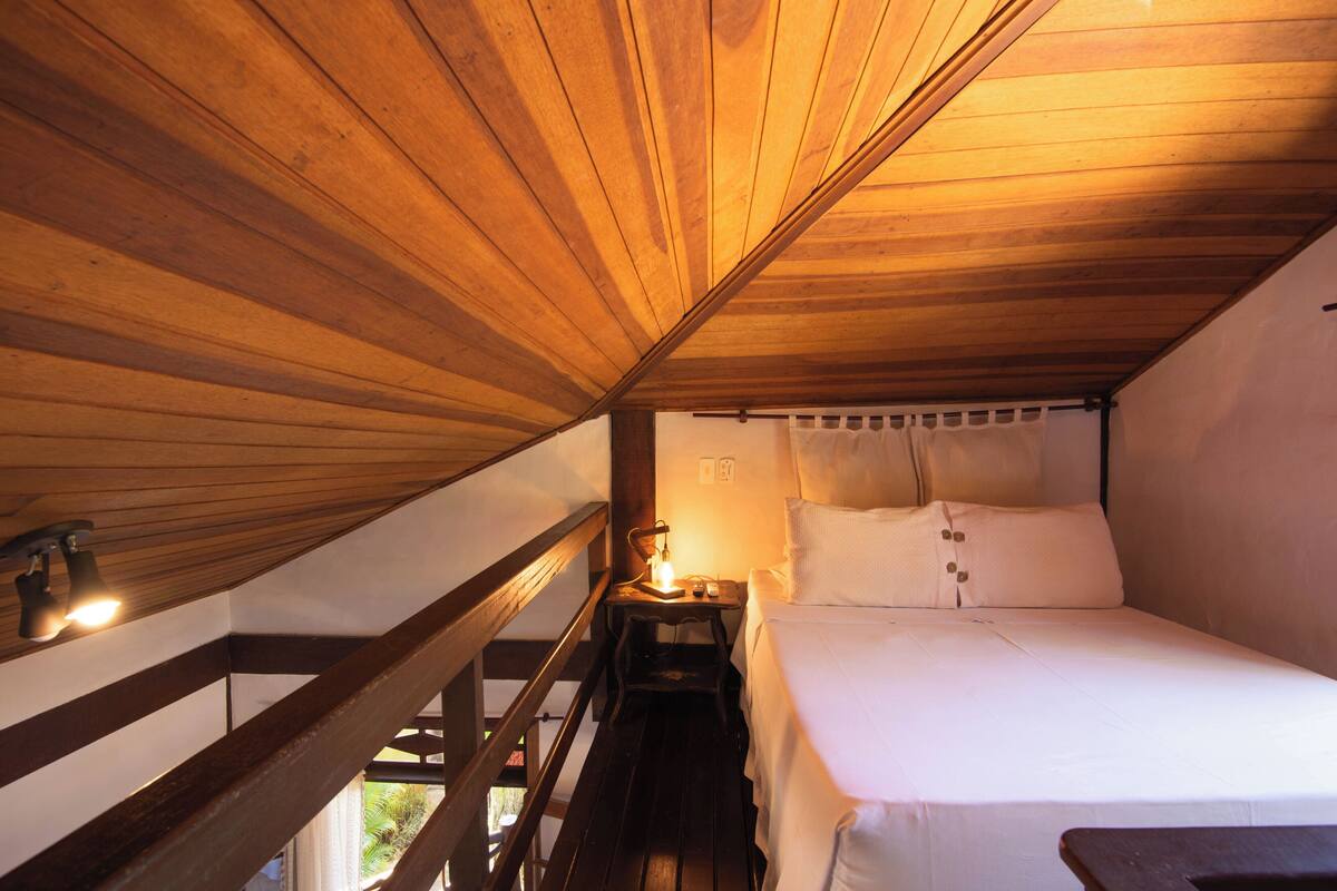 Ein Schlafzimmer mit Holzboden, einem Bett mit weißen Leinen, einem Nachttisch und einem Fenster mit Vorhängen.