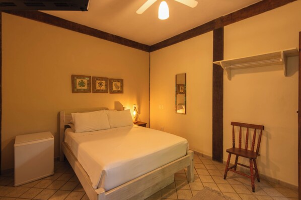 Un dormitorio con cama, una silla, una mesita de noche, un espejo y estante en la pared.