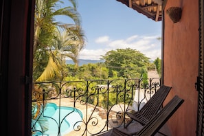 A balcony with a view of a swimming pool, palm trees, and a distant landscape. - Pousada Villaggio Assis (Ilhabela)
