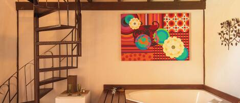 A bathroom with a wooden bathtub, a metal spiral staircase, and a colorful abstract painting on the wall.