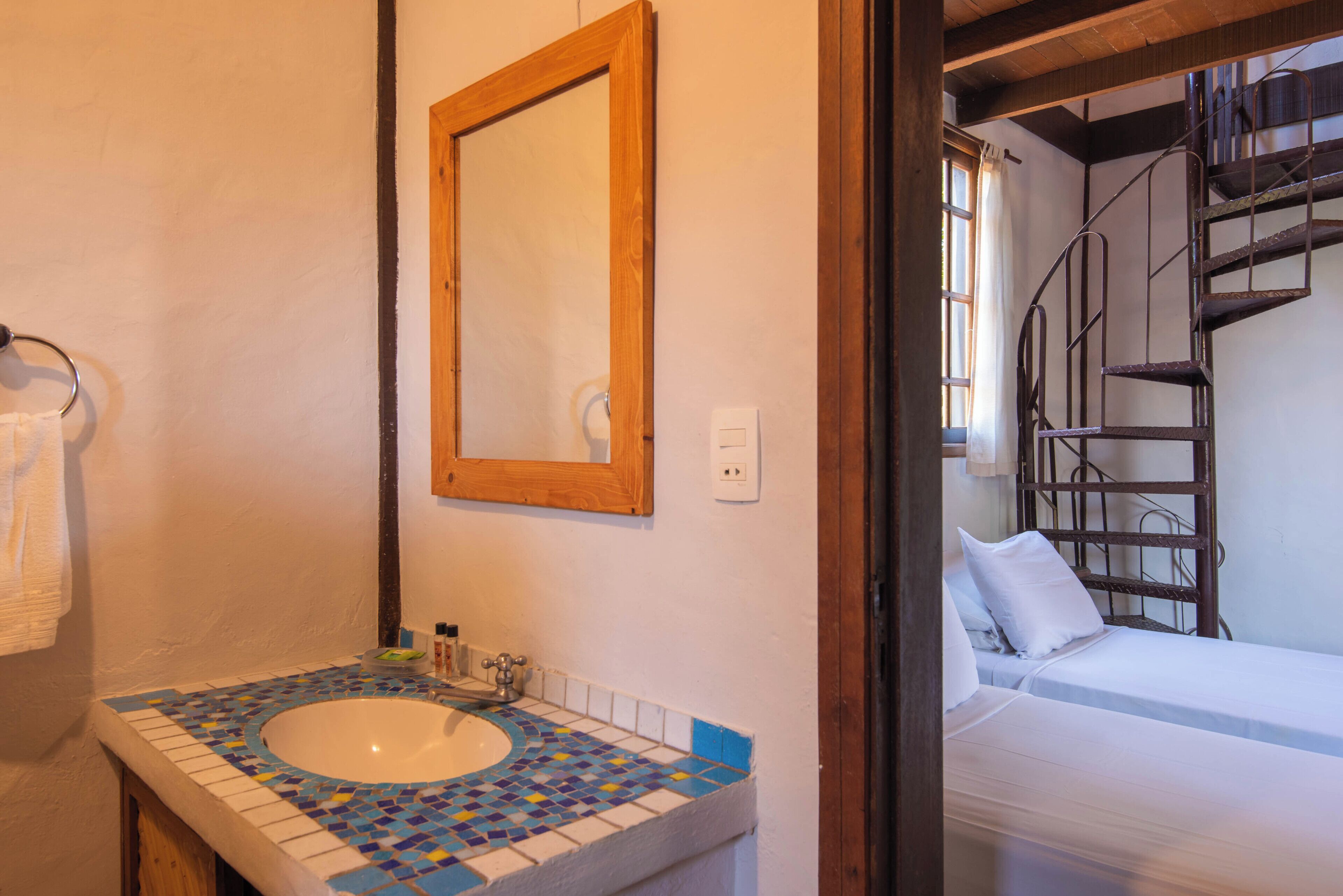 A bathroom with a mosaic sink, a wooden-framed mirror, and a white towel hanging on the wall.