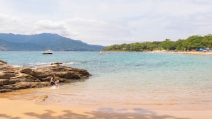 Una playa con agua cristalina, costa rocosa y montañas al fondo.