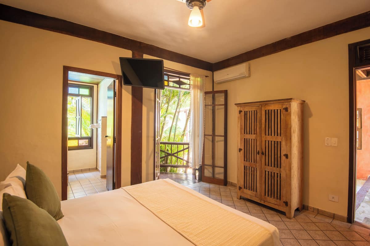 Ein Schlafzimmer mit einem Bett, einem an der Wand montierten Fernseher, einem Holzschrank und einer Tür, die auf einen Balkon führt.