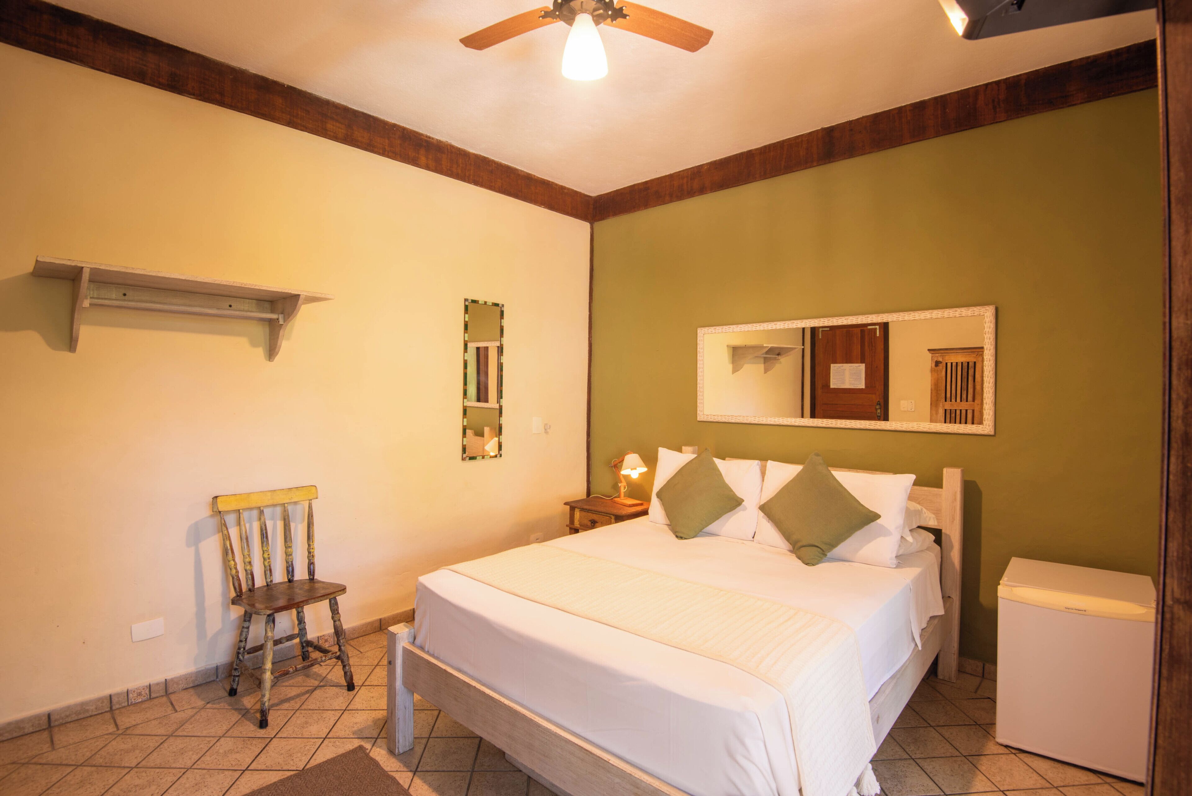 A bedroom with a bed, a chair, a nightstand, a mirror, and a ceiling fan.