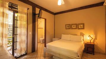 Un dormitorio con cama, mesita de noche, lámpara, ventilador de techo y vistas al exterior a través de una puerta.