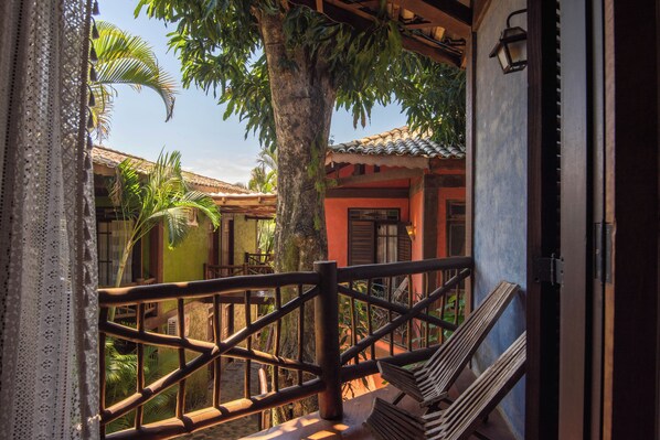 A wooden balcony with a railing, a bench, and a view of a building with a tiled roof. - Pousada Villaggio Assis (Ilhabela)