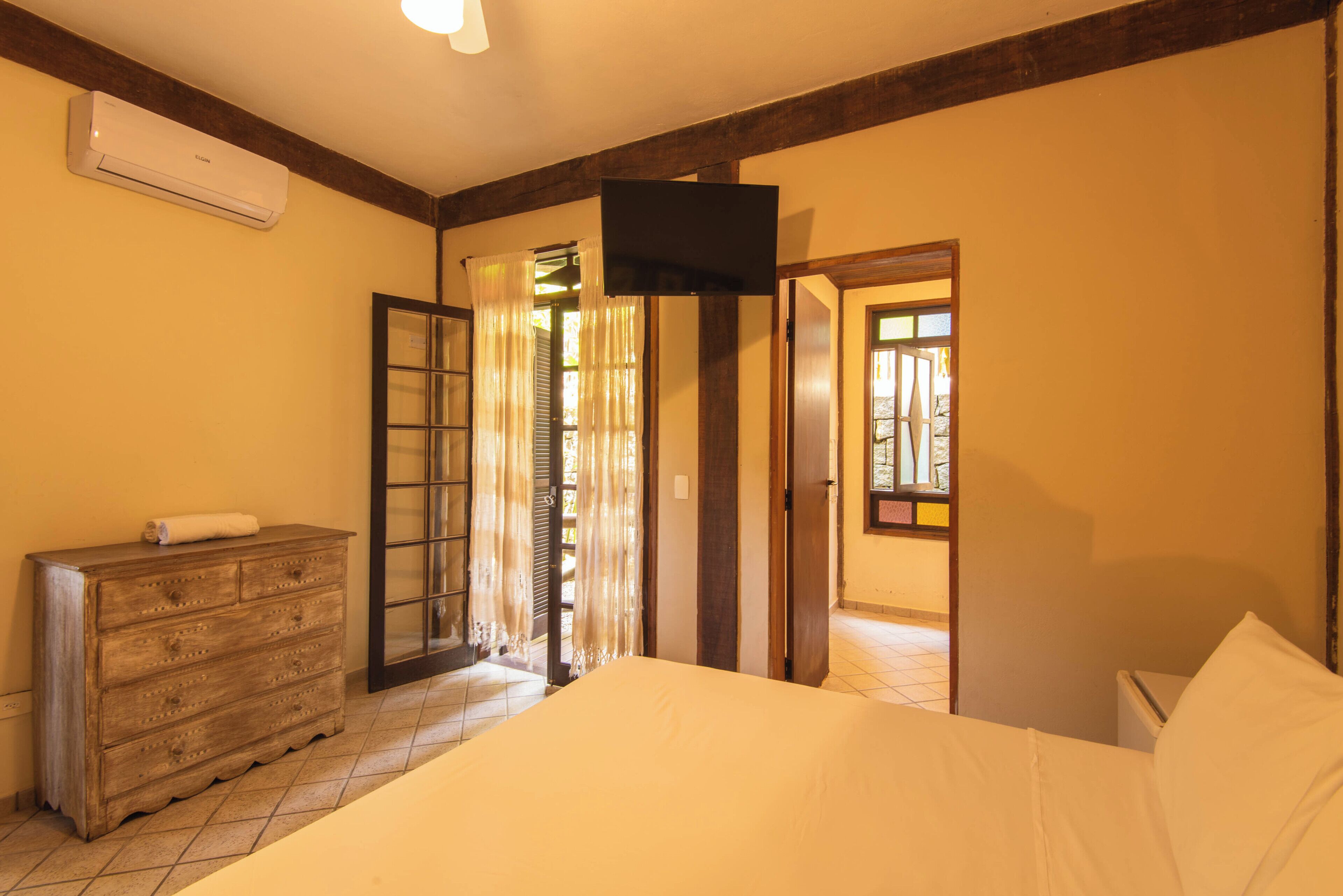 Ein Schlafzimmer mit einem Bett, einer Kommode, einem Fernseher und einer Tür zu einem weiteren Raum.