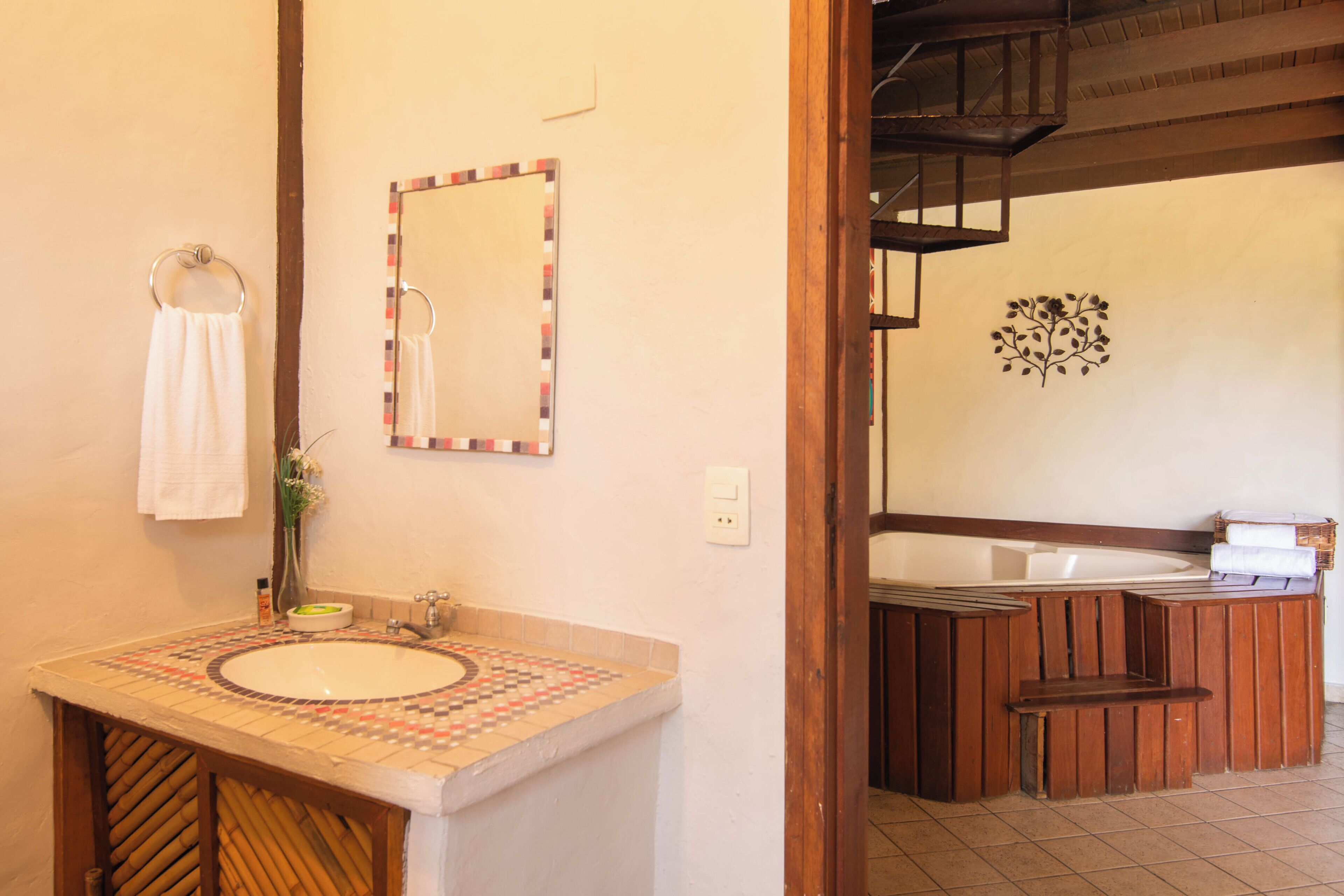 A bathroom with a sink, mirror, towel rack, and a wooden bench.