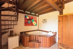 A corner room with a wooden bathtub, a wooden cabinet, a spiral staircase, and a colorful wall decoration. - Pousada Villaggio Assis (Ilhabela)