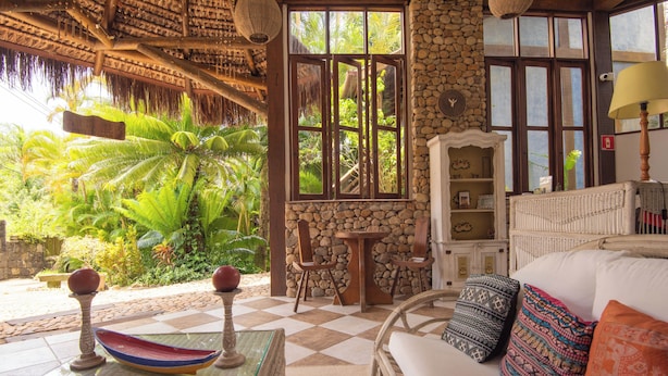 Una habitación con piso a cuadros, un sofá de mimbre, una mesa de vidrio con un cuenco decorativo, una pared de piedra y vistas a follaje tropical.