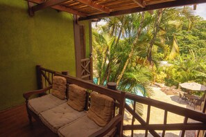 A wooden bench with cushions, a wooden railing, and a view of a tropical garden with palm trees.