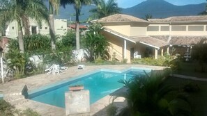 A swimming pool surrounded by palm trees and buildings with a mountainous backdrop. - Hotel Portal de Barequeçaba (São Sebastião)