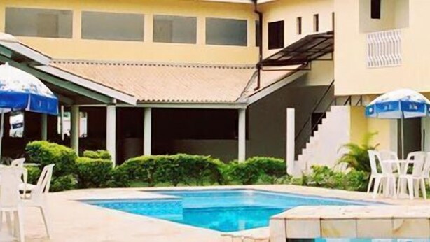 A hotel pool area with a swimming pool, white lounge chairs, and blue umbrellas. - Hotel Portal de Barequeçaba (São Sebastião)