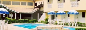 A hotel pool area with a swimming pool, white lounge chairs, and blue umbrellas. - Hotel Portal de Barequeçaba (São Sebastião)