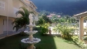 A courtyard with a central fountain, surrounded by greenery and a building with a balcony. - Hotel Portal de Barequeçaba (São Sebastião)