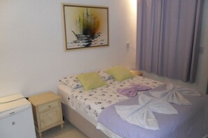 Un dormitorio con cama, almohadas, una mesita de noche, un electrodoméstico pequeño y un cuadro en la pared.
