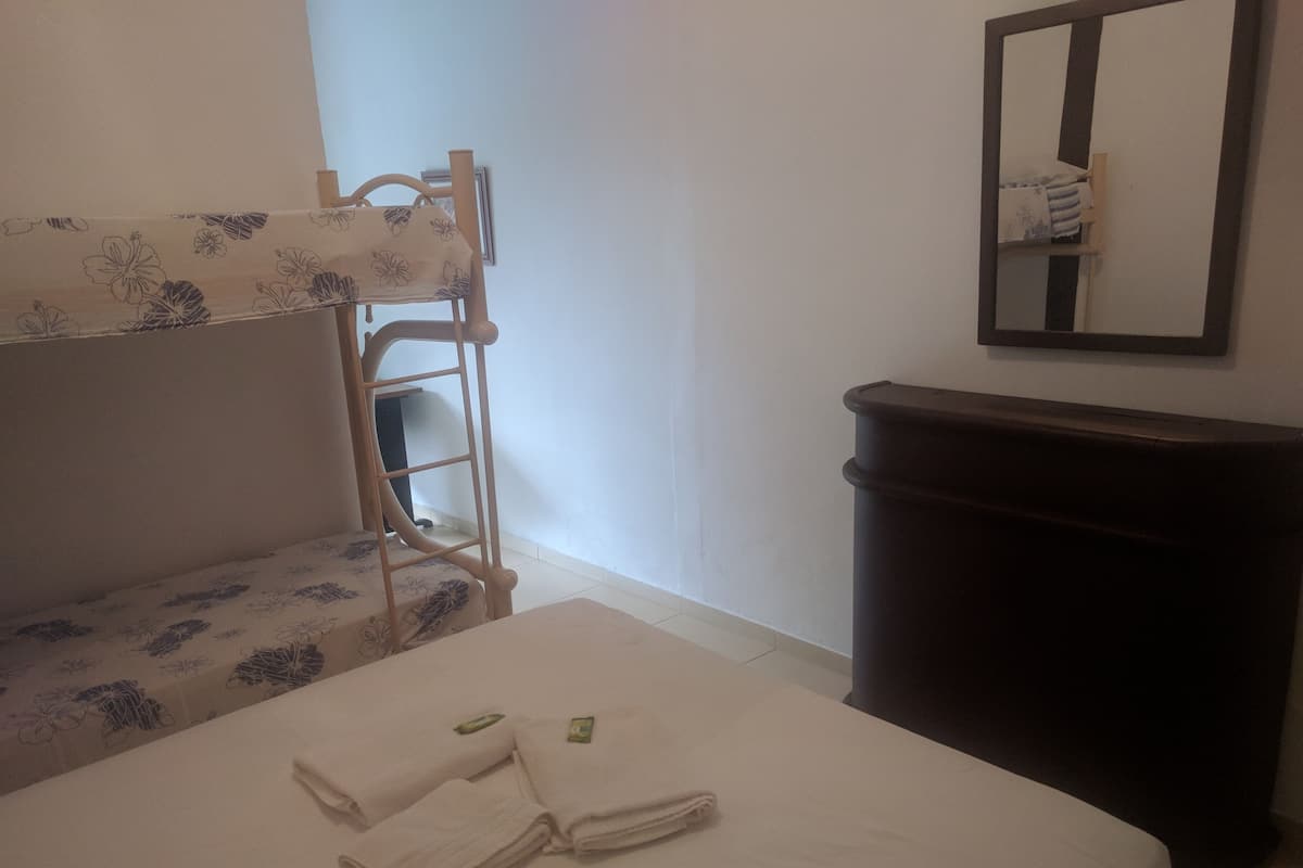 Um quarto com uma cama de solteiro, uma mesinha com toalhas, uma lixeira e um espelho na parede.