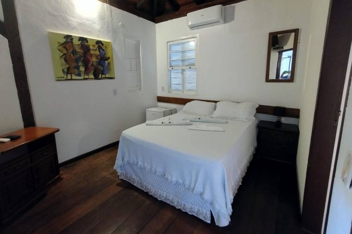 Quarto com cama, mesas de cabeceira, penteadeira, um armário e um ar condicionado.