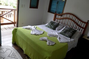 A room with a bed, a wooden headboard, a green bedspread, and a white doily on the floor.