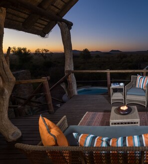 Une terrasse extérieure aménagée avec des meubles en osier et une piscine, offrant une vue sur un paysage désertique au crépuscule.