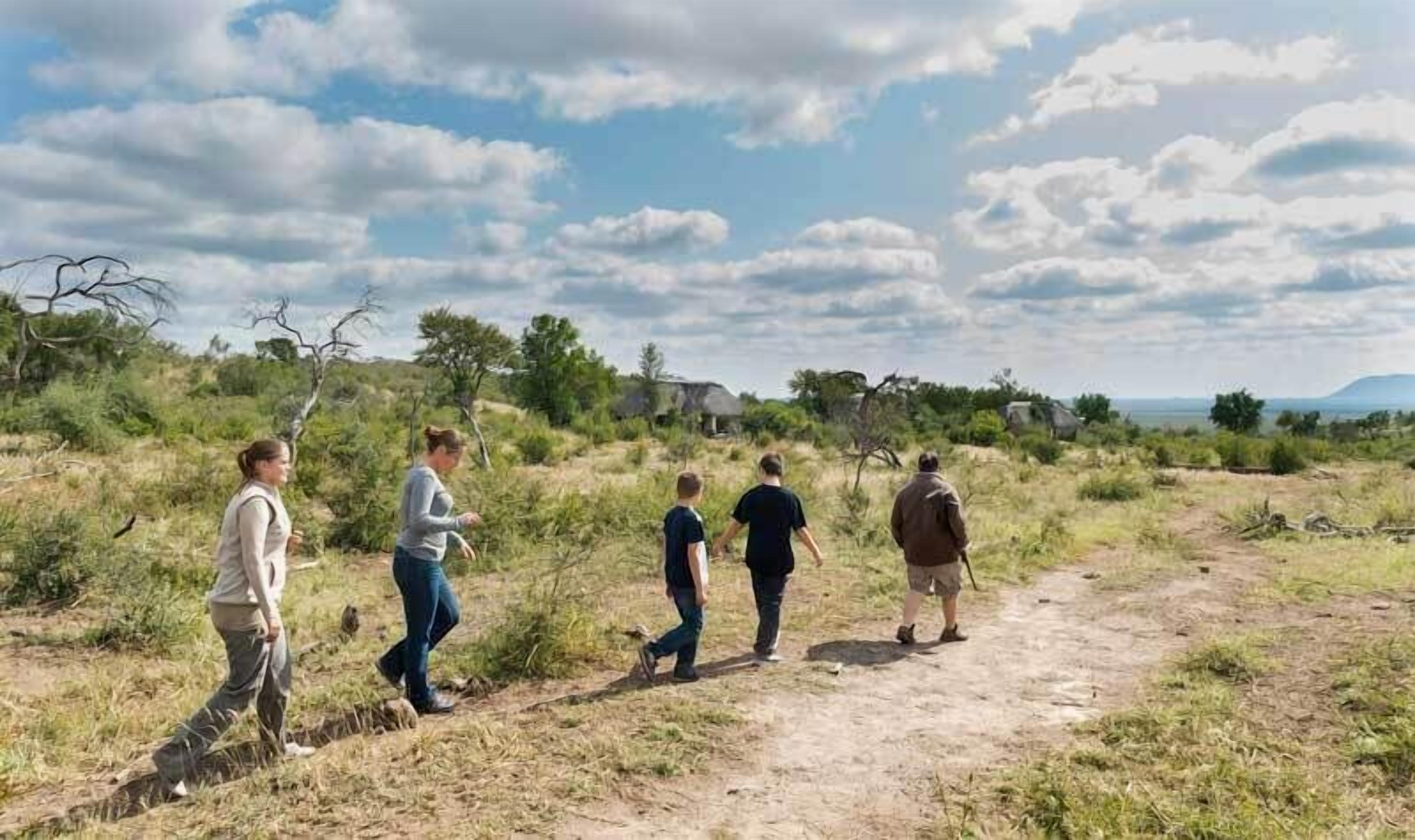 A group of people walking on a dirt path in a natural setting with sparse vegetation and a clear sky.