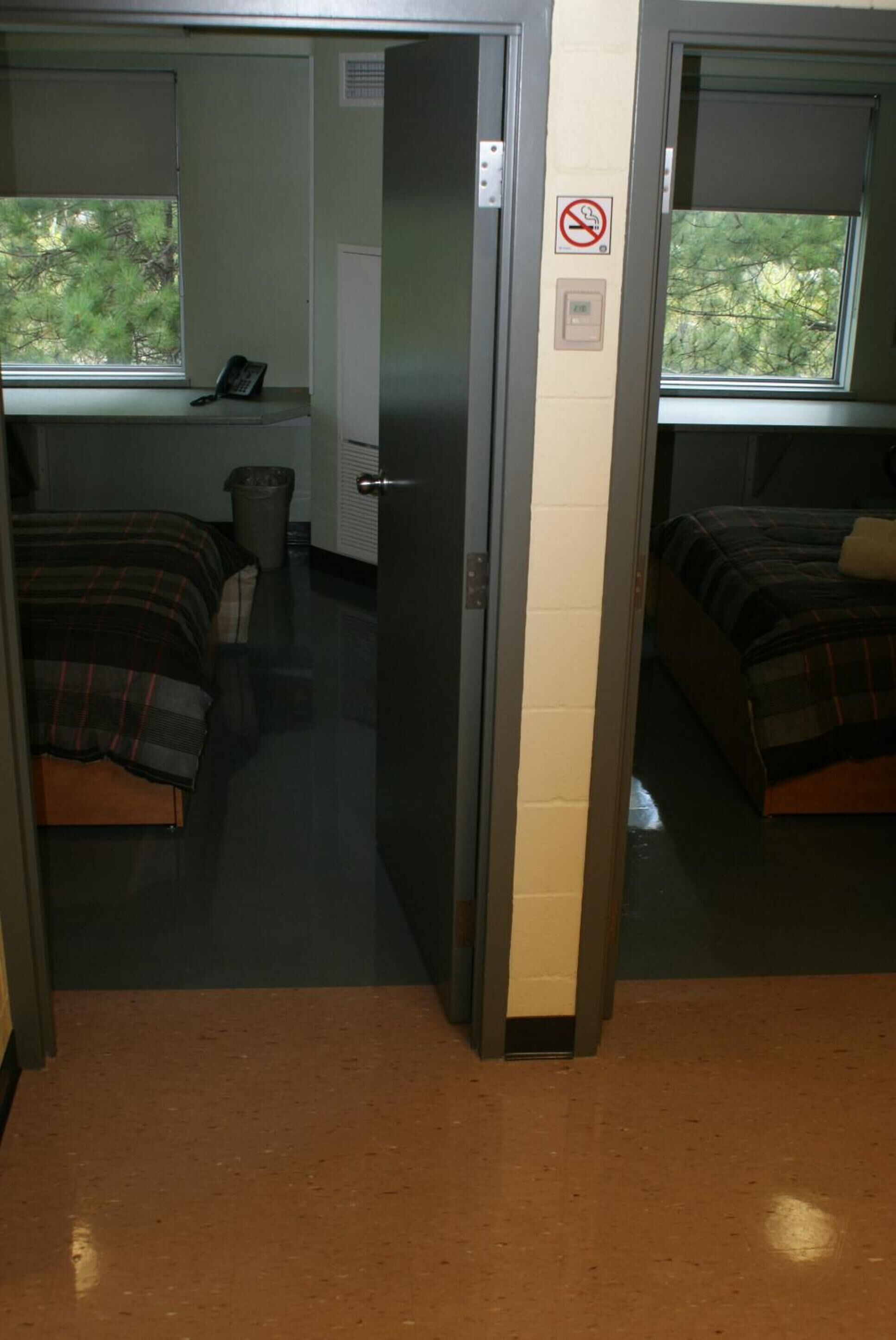 A dormitory room with two beds, a desk, a chair, and a window.
