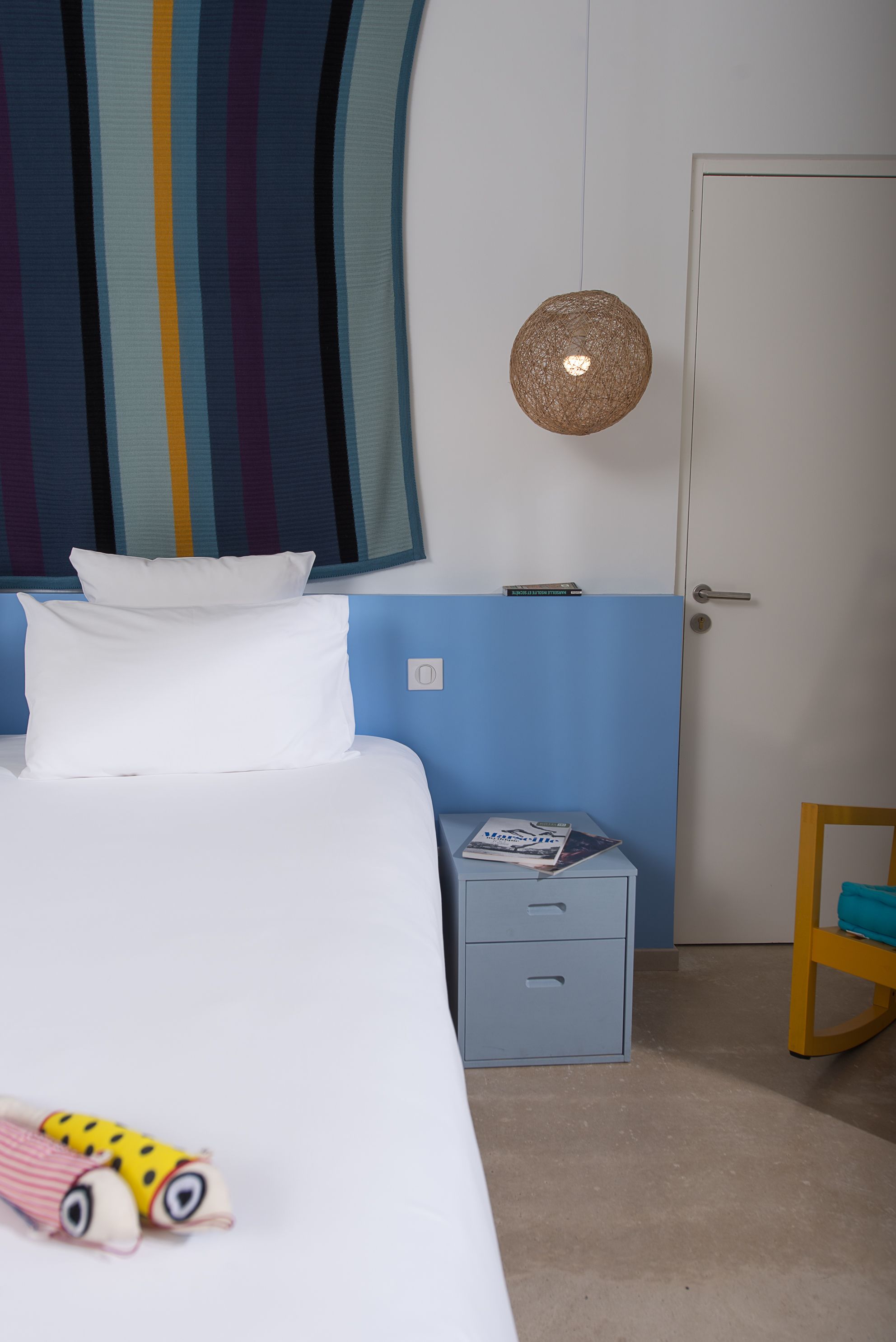 Une chambre à coucher avec un lit, une table de chevet, une chaise, une porte et un mur sur lequel est accroché un rideau à rayures.