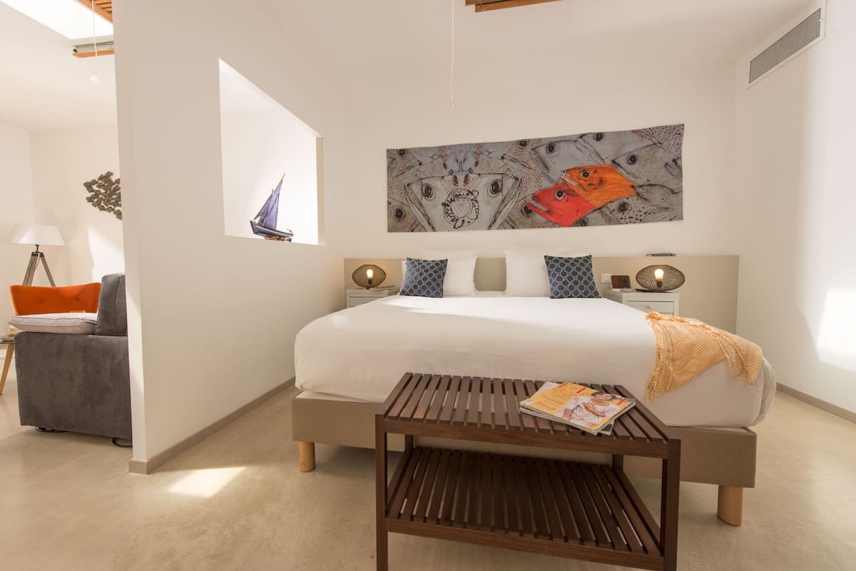 A modern bedroom with a large bed, a wooden side table, a wall-mounted artwork, and a window with a sailboat view.