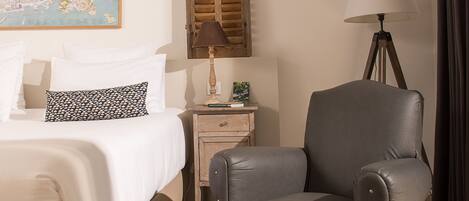 Habitación de hotel con cama, un sillón gris, mesita de noche con lámpara y un mapa en la pared.
