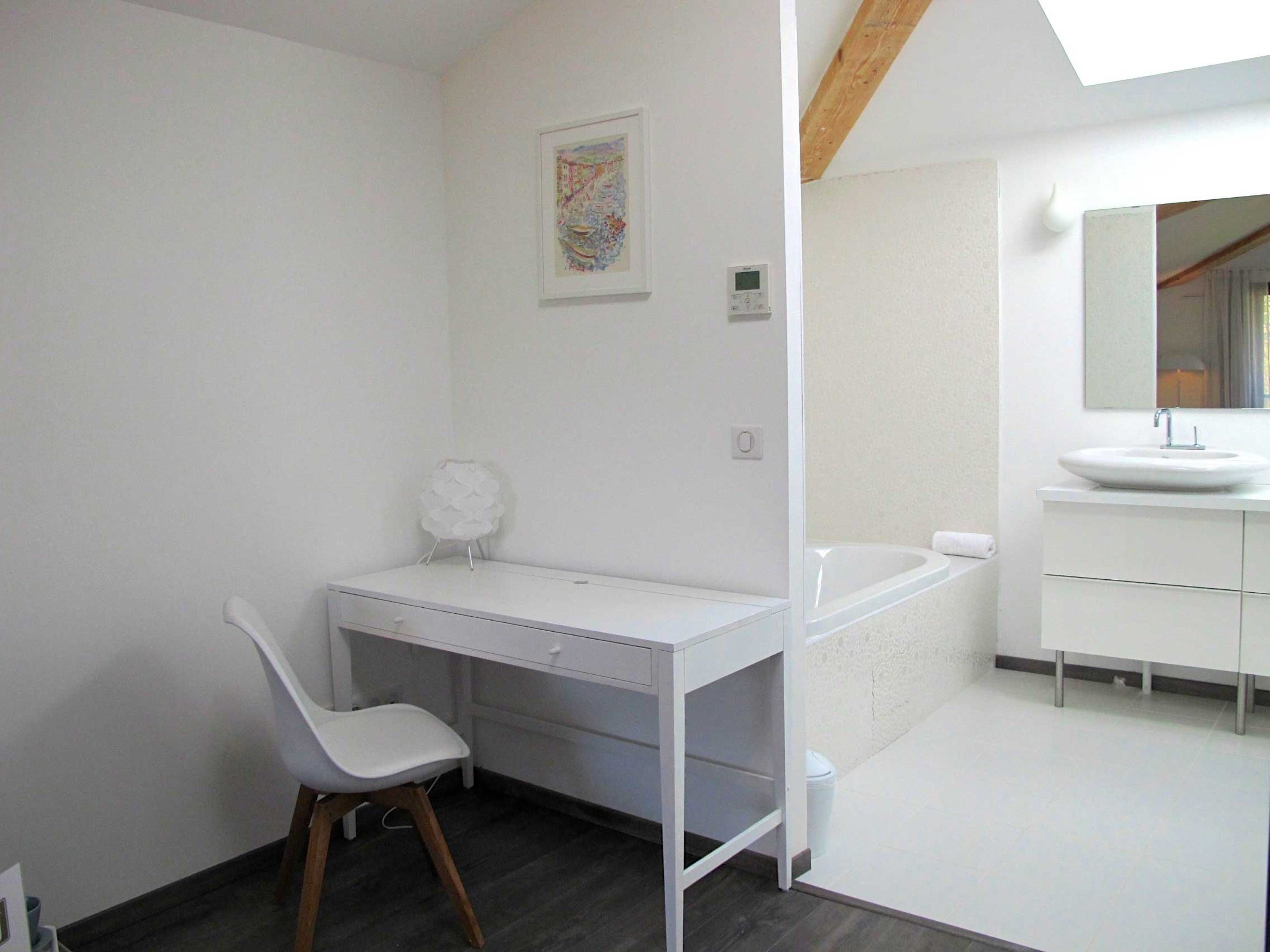 Een moderne badkamer met een wit wastafelmeubel, een badkuip en een klein bureau met een stoel.