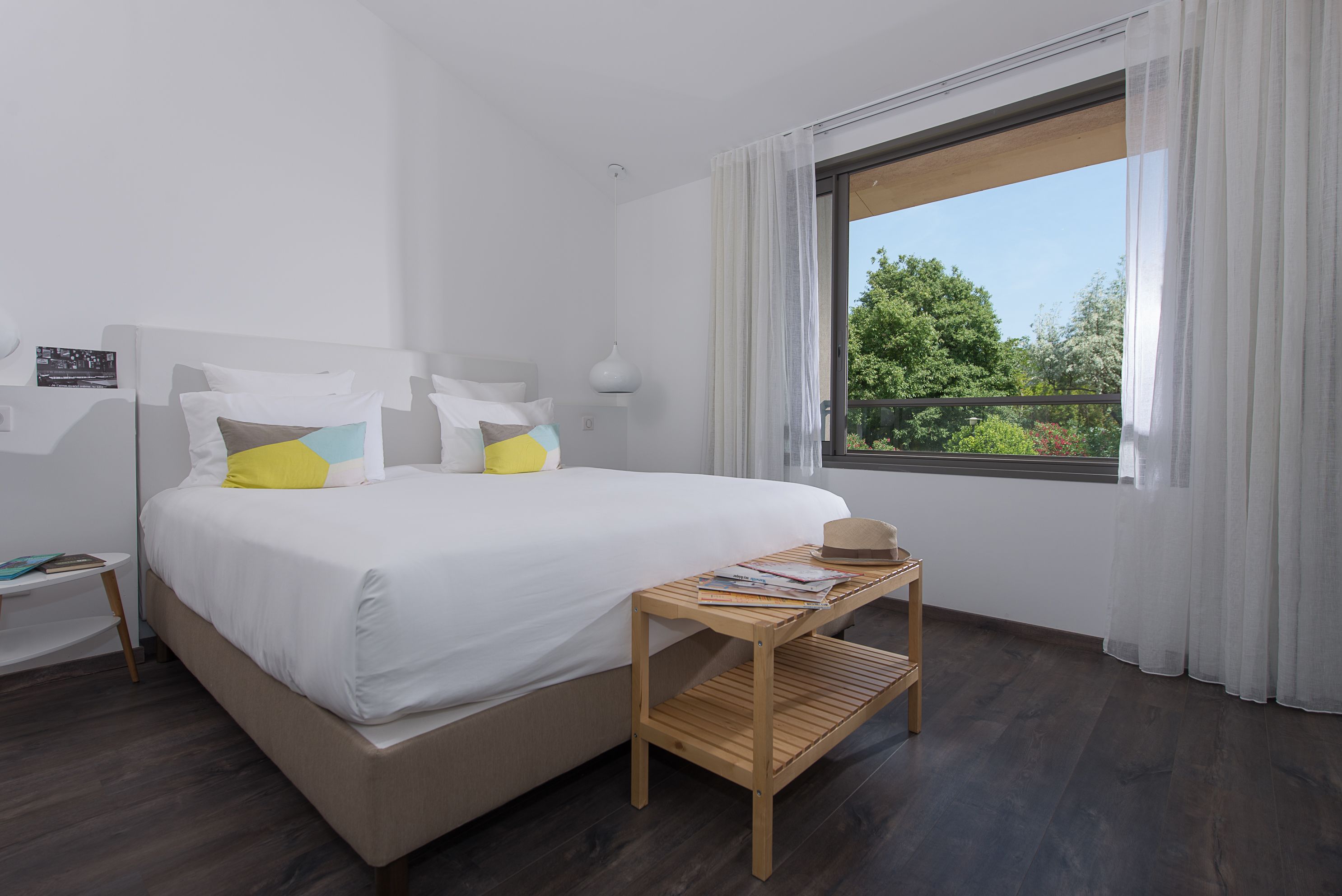 Una habitación de hotel moderna con una cama grande, una mesita de noche de madera y una ventana con vistas a zonas verdes.