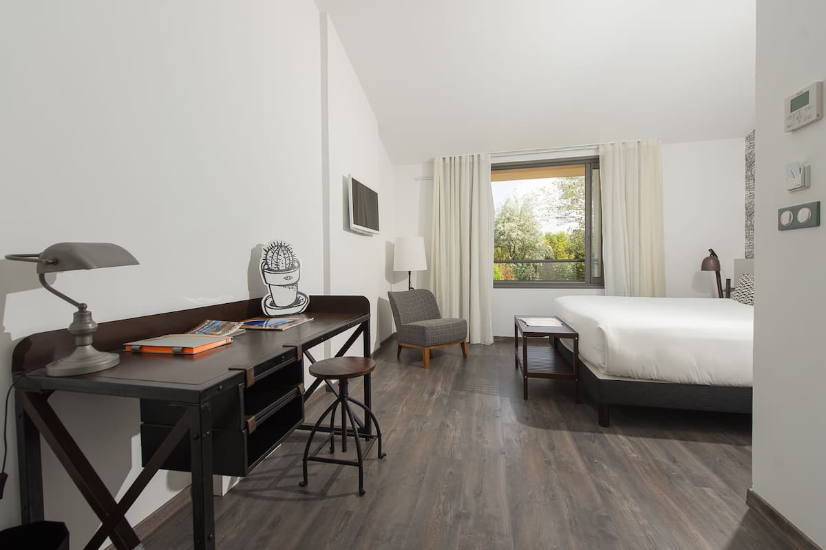 A hotel room with a bed, desk, chair, and a window with curtains.