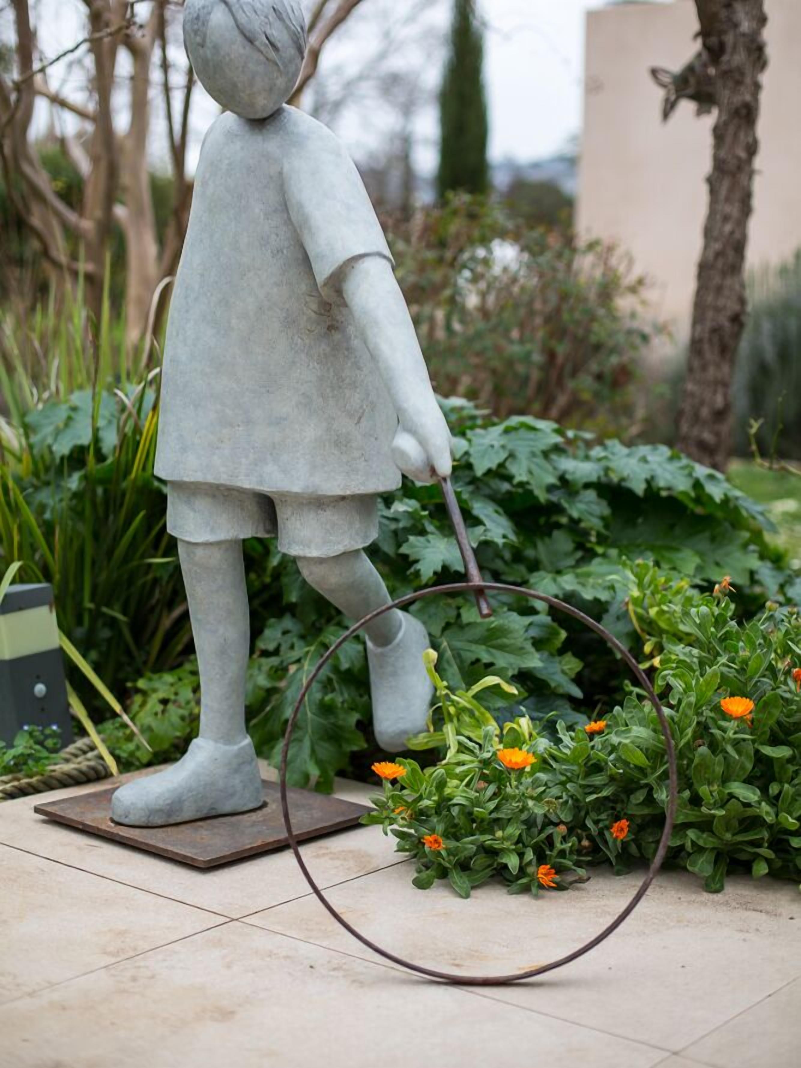 A statue of a child holding a hoop in a garden setting.