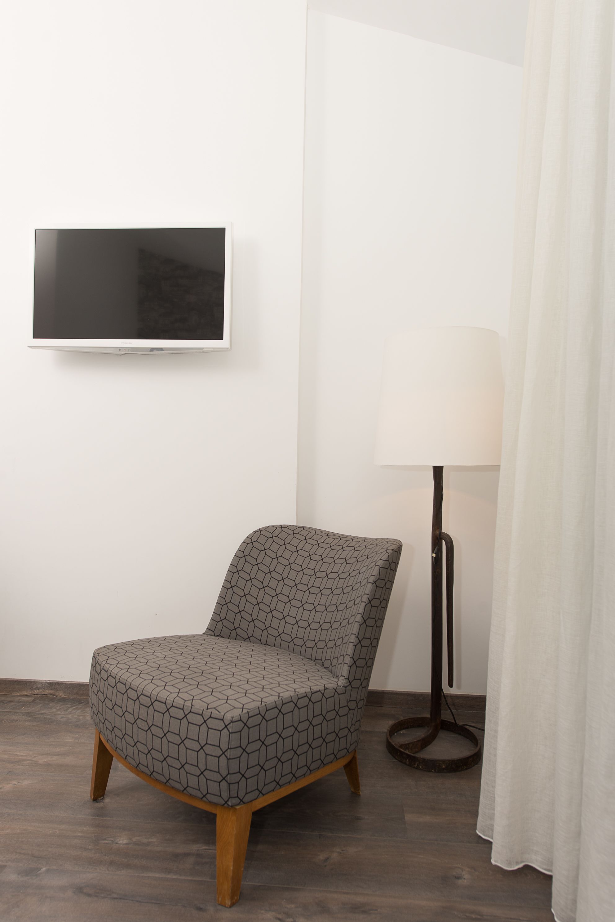 A modern room with a hex-patterned chair, a floor lamp, and a flat-screen TV mounted on the wall.