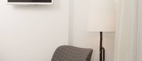 A modern room with a hex-patterned chair, a floor lamp, and a flat-screen TV mounted on the wall.