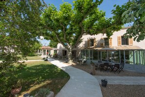 A covered patio area with outdoor furniture, a pathway, and a large tree providing shade. - Hotel 96 (Marseille)
