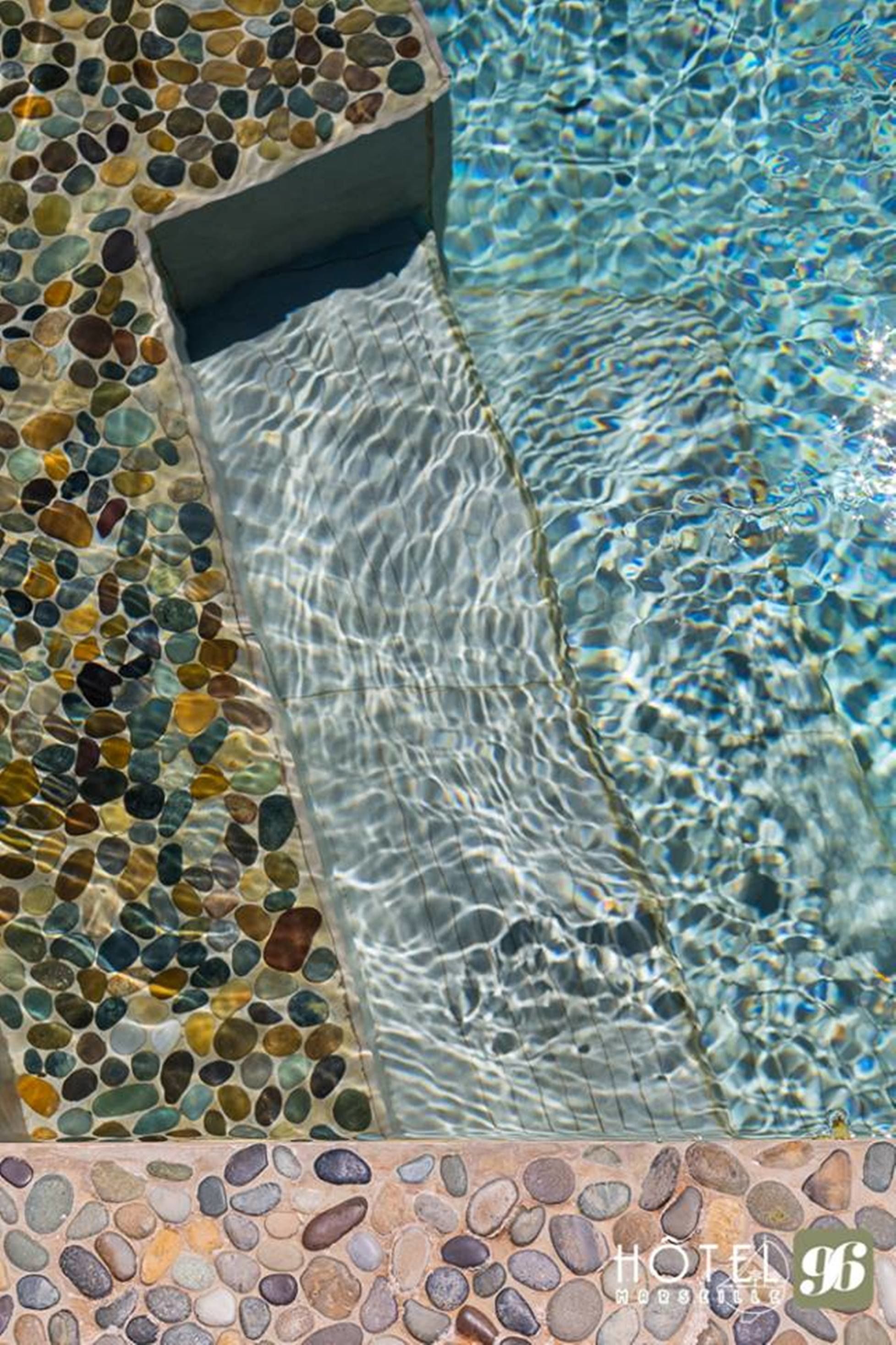 Une piscine bordée de mosaïques et dont l’eau est d’une clarté parfaite.