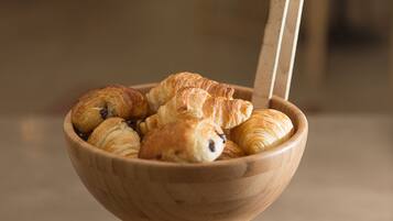 Een houten kom met een lepel, gevuld met croissants.