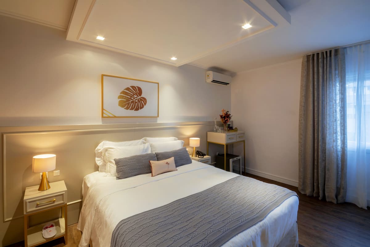 Ein Hotelzimmer mit einem großen Bett, Nachttischen, einem Schreibtisch und einem Fenster mit Vorhängen.