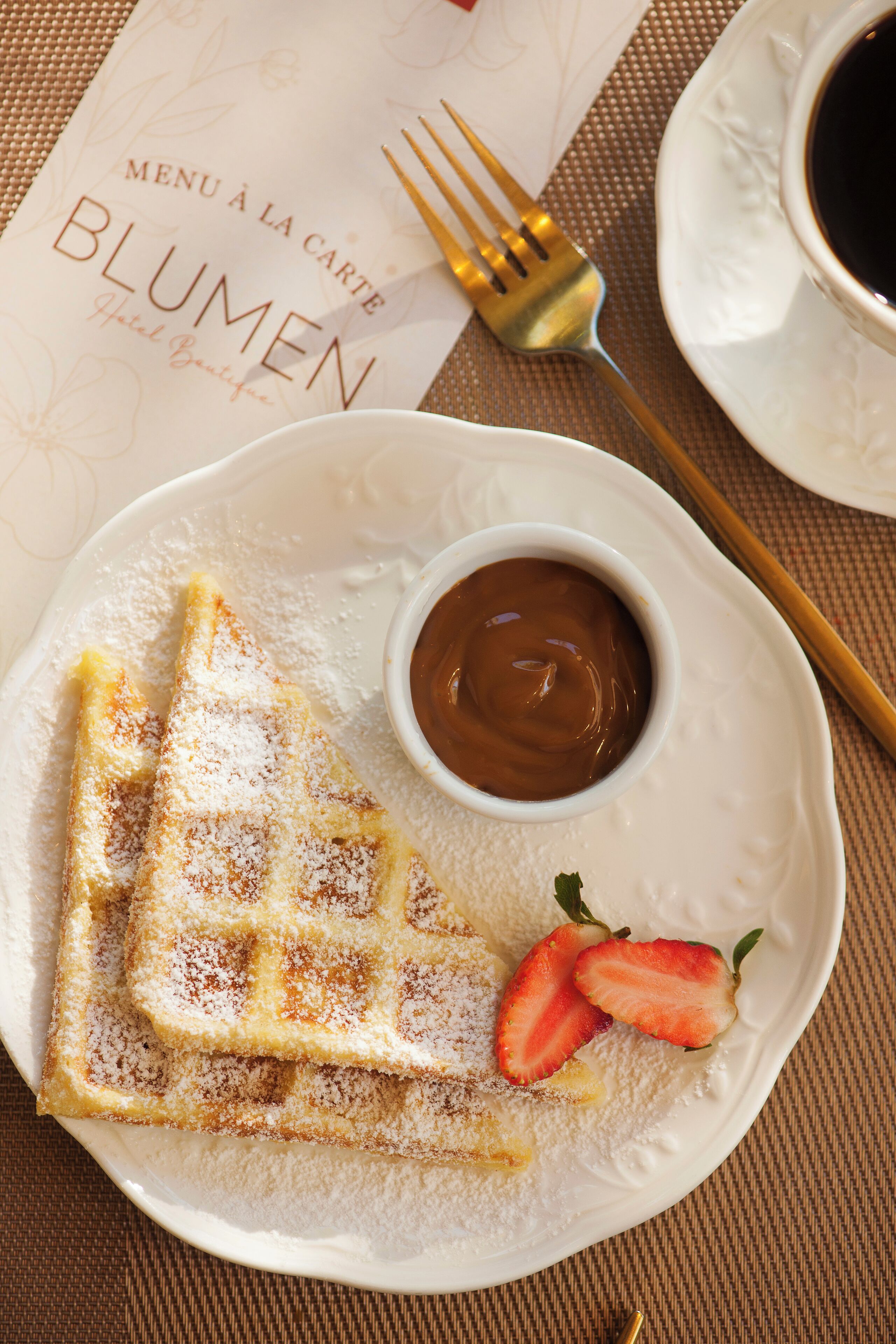 Ein Teller mit Pfannkuchen, bestäubt mit Puderzucker und Schokoladensauce, dazu Erdbeeren und eine Speisekarte.