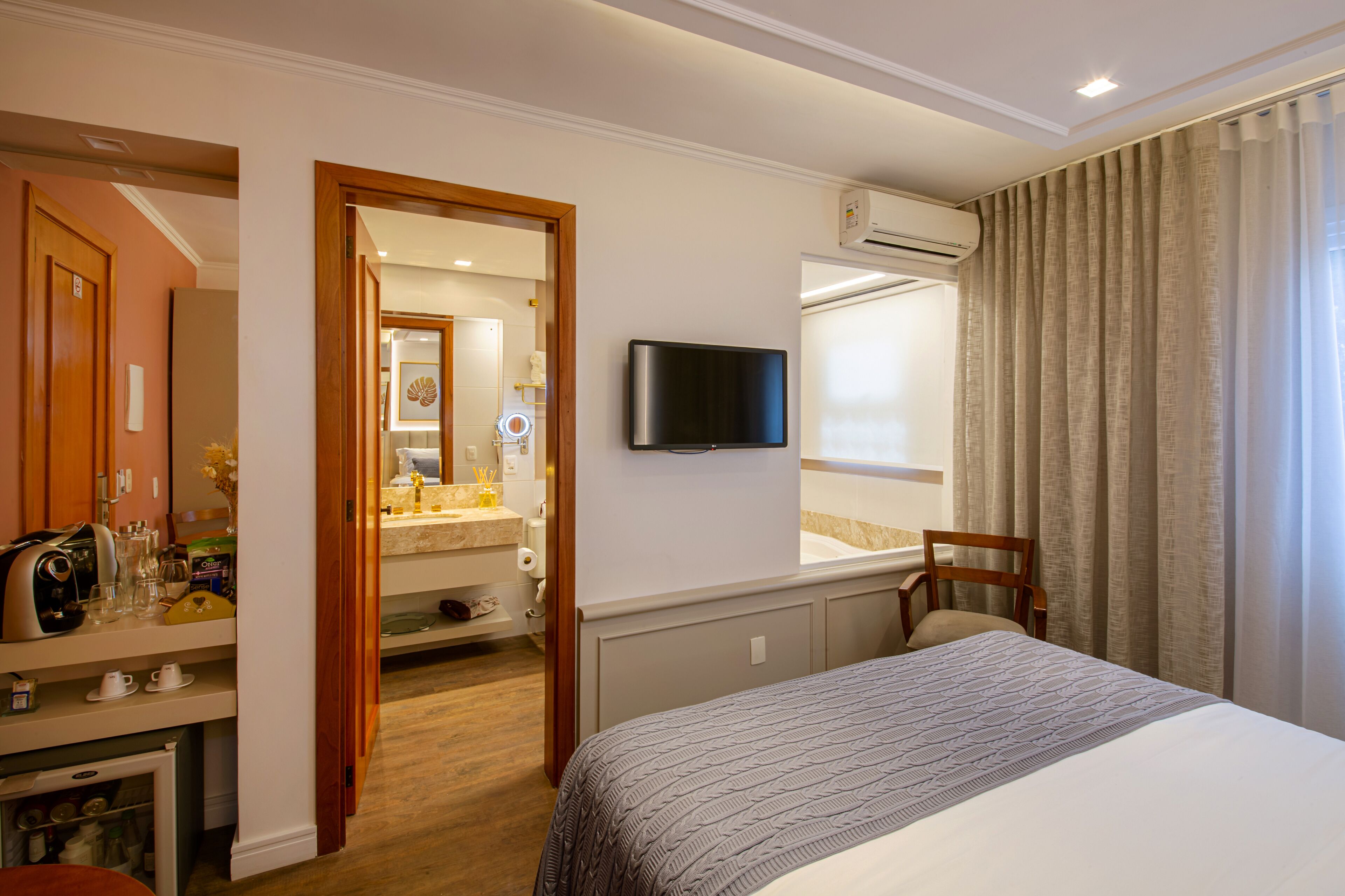 Habitació d'hotel amb un llit, una televisió, un escriptori amb un ordinador, una cadira i un bany visible a través d'una porta oberta.