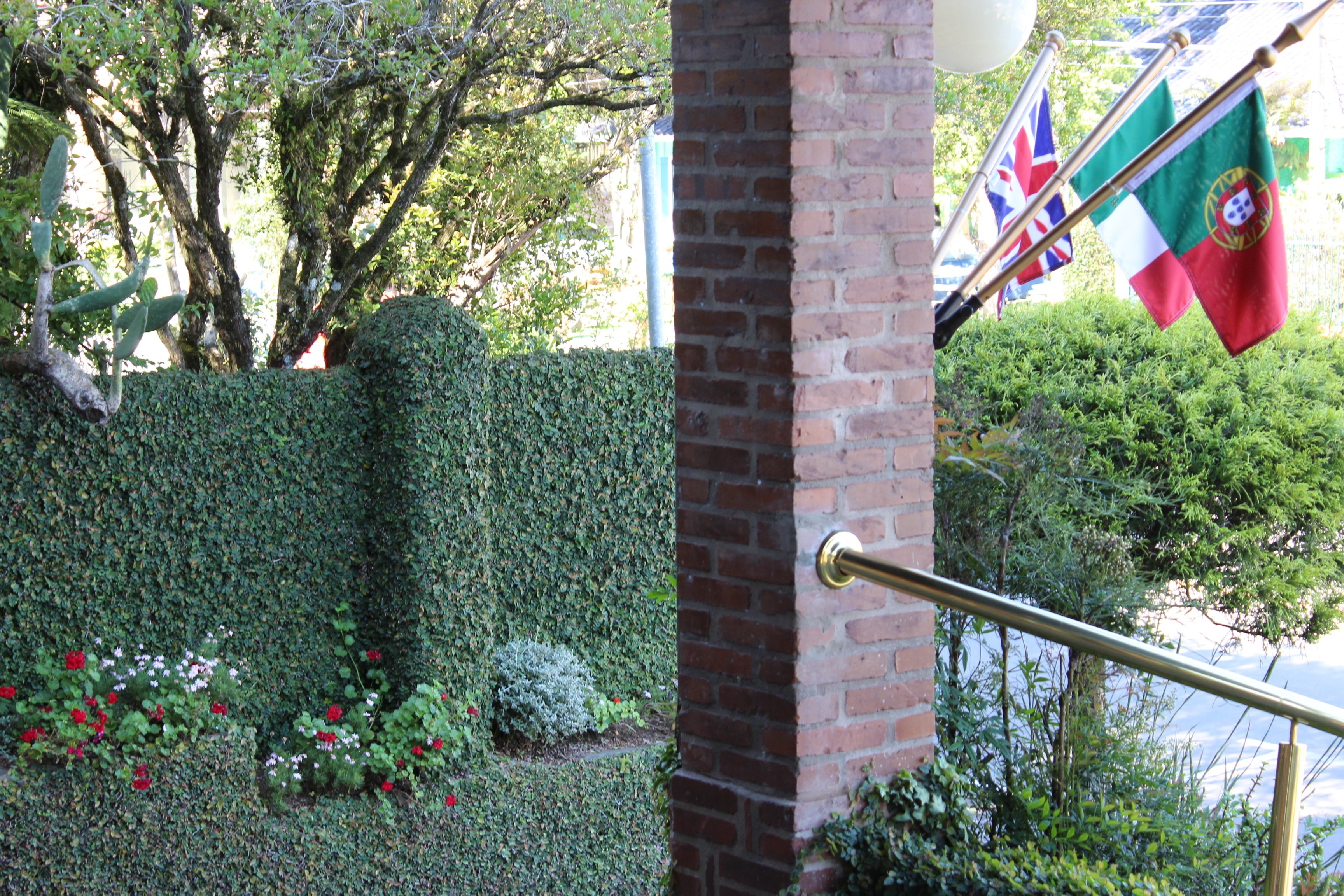 A brick wall with a metal railing, a hedge, and flags.