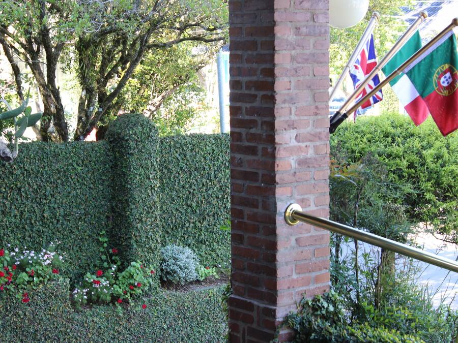 A brick wall with a metal railing, a hedge, and flags.